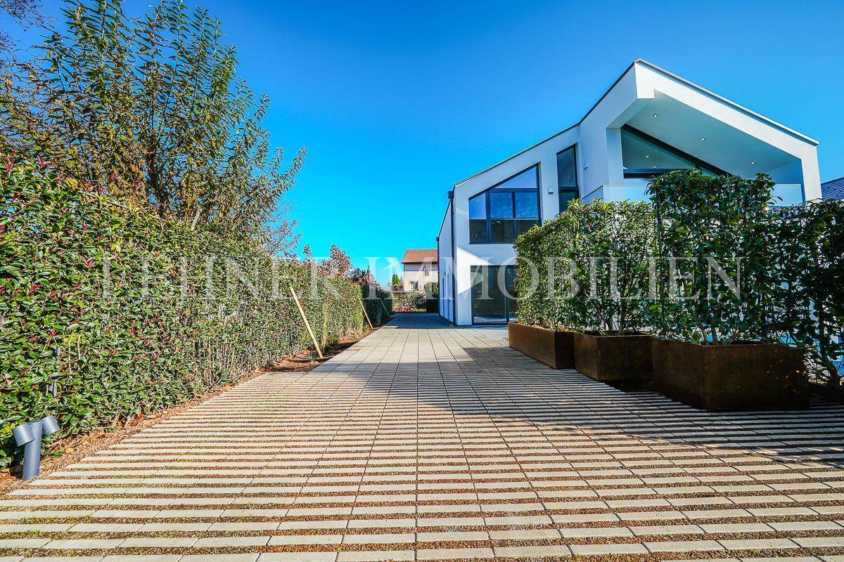Langer gepflasterter Zufahrtsweg zur modernen Villa, umgeben von hohen Hecken.