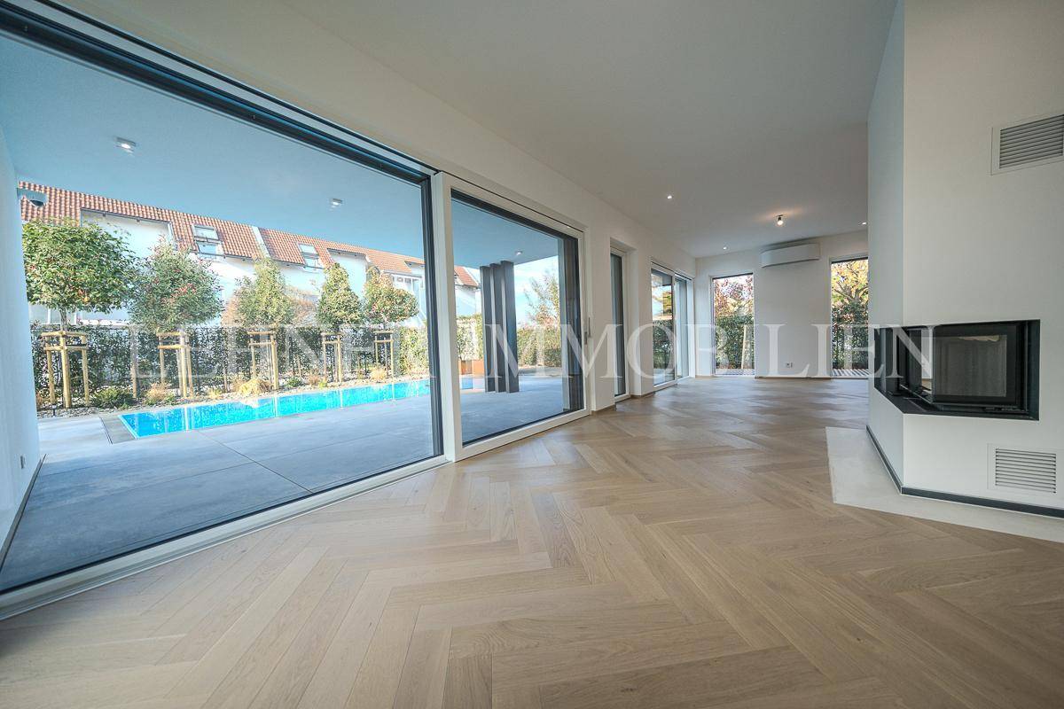 Großzügiger Wohnraum mit raumhohen Fenstern, die den Blick auf den Pool und den Garten freigeben.