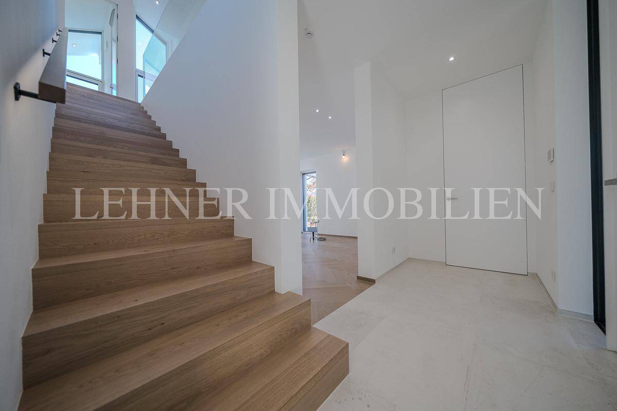 Moderner Eingangsbereich mit eleganter Holztreppe und hellem Fliesenboden.