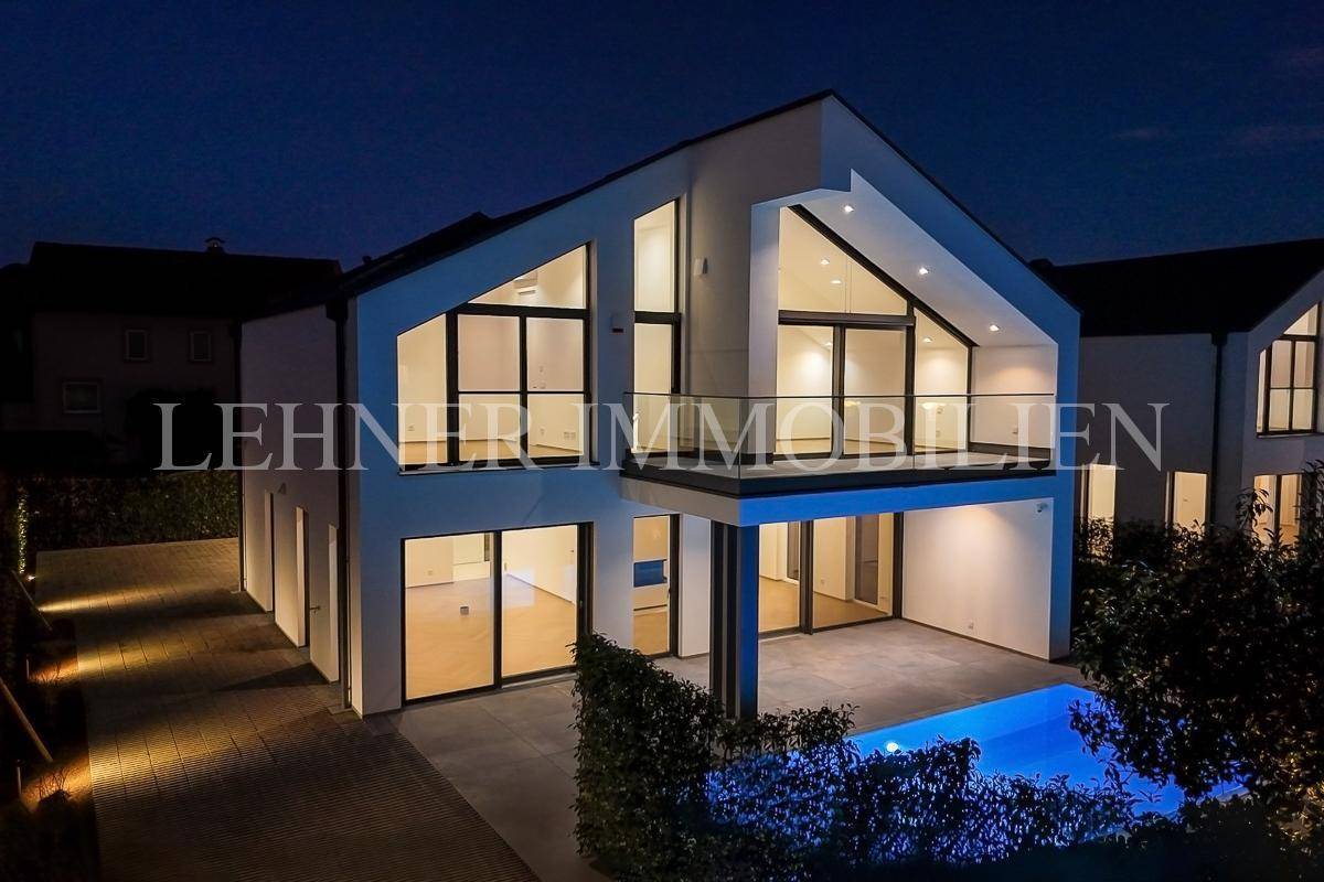 Elegante moderne Villa bei Nacht mit beleuchtetem Poolbereich und großzügigen Fensterfronten.