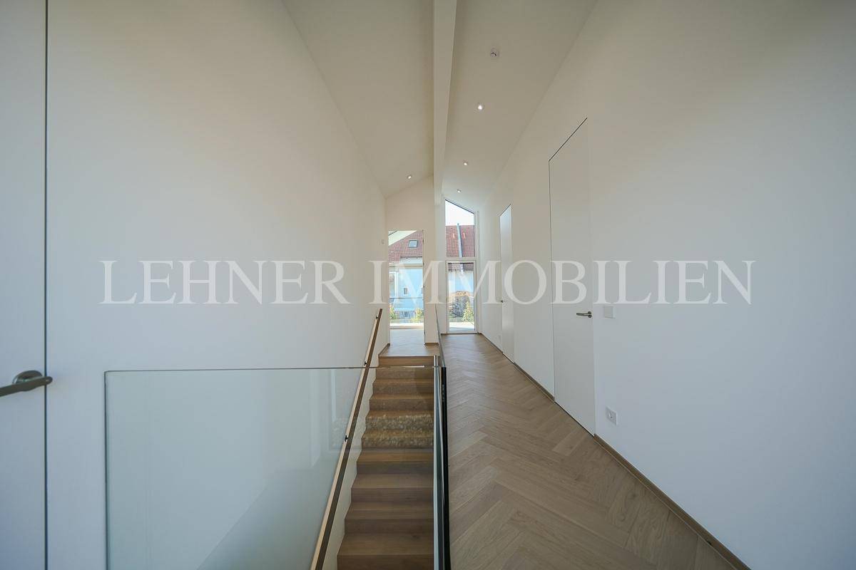 Langer, heller Flur mit Fischgrätparkett, moderner Treppe und viel Tageslicht.