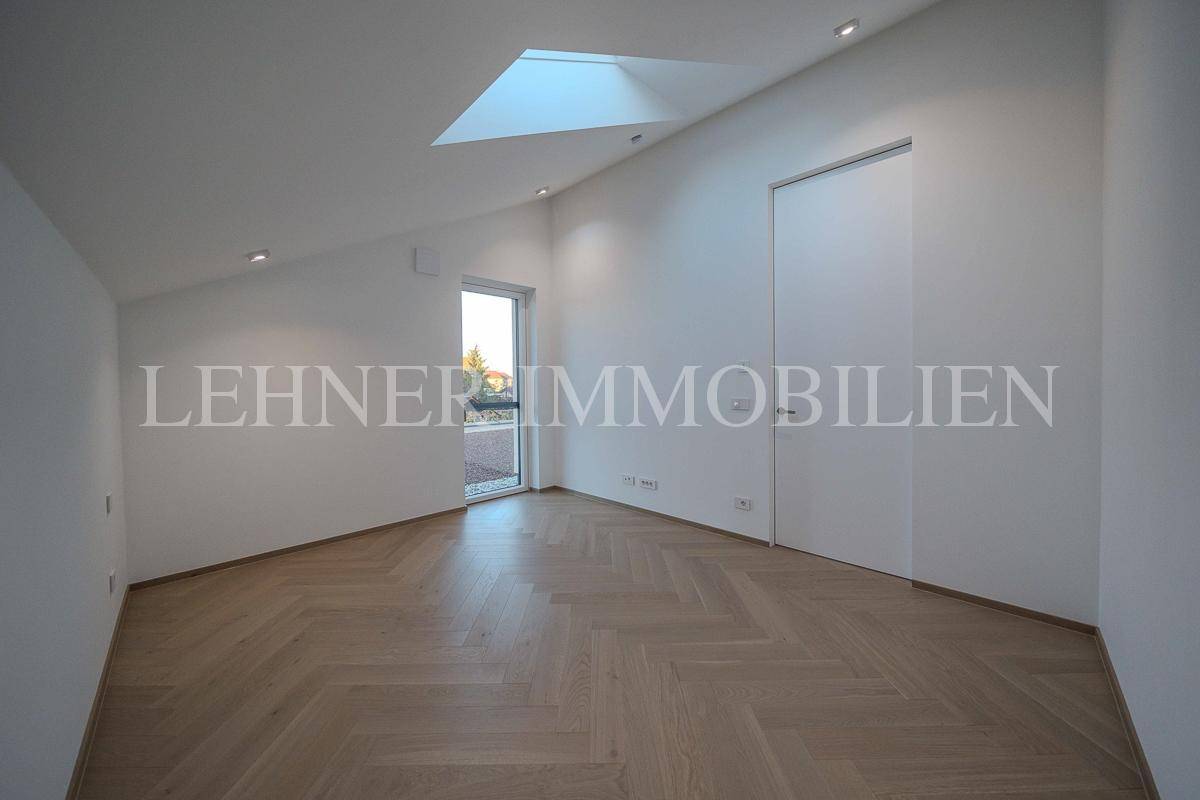 Heller Raum mit Fischgrätparkett, schräger Decke und Dachfenster, bietet Zugang zu einem Außenbereich.