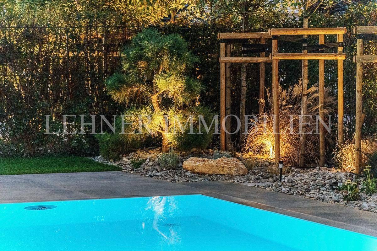 Detailansicht des gepflegten Gartens mit Beleuchtung und dem Rand des leuchtenden Pools.