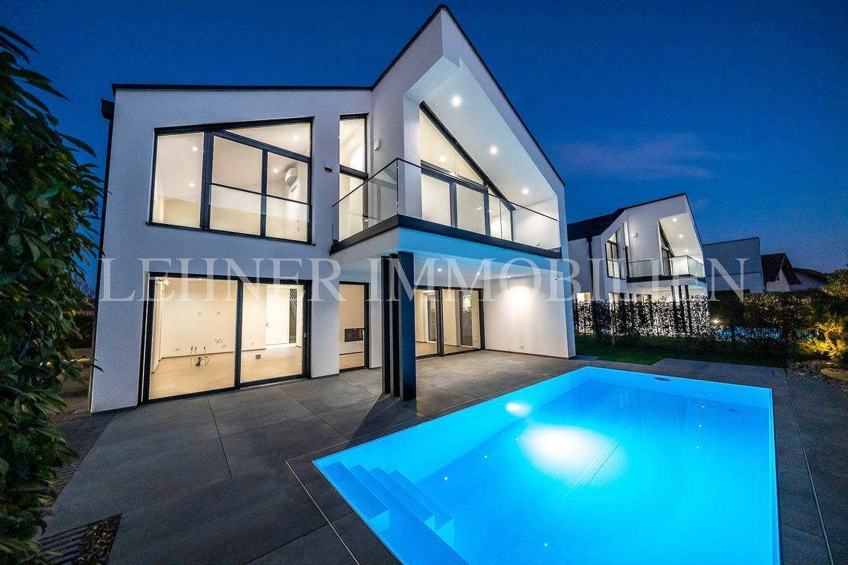 Beeindruckende moderne Villa mit leuchtendem Pool und weitläufigen Glasflächen in der Abenddämmerung.