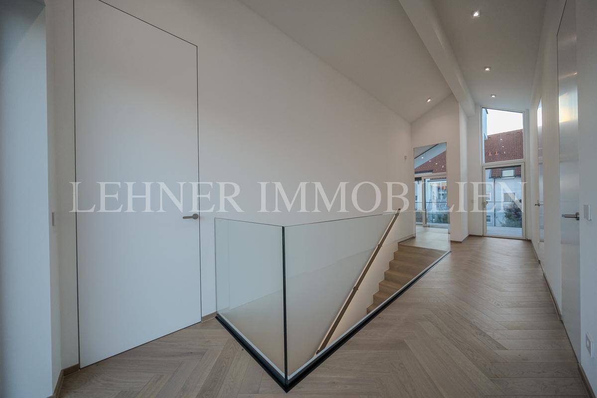 Heller Flur mit Fischgrätparkett, minimalistischen Türen und modernem Glasgeländer.