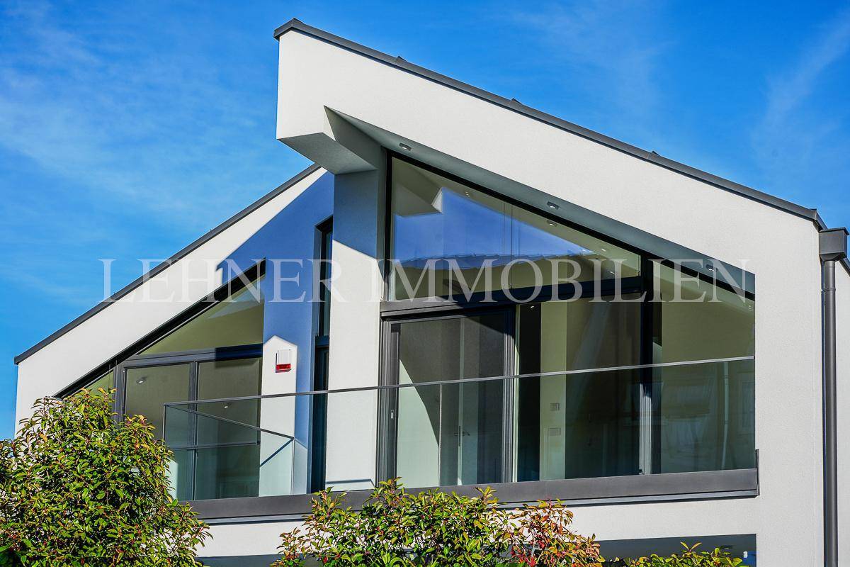 Zeitgenössische Fassade mit markanten Giebelfenstern und Balkon mit Glasbrüstung.