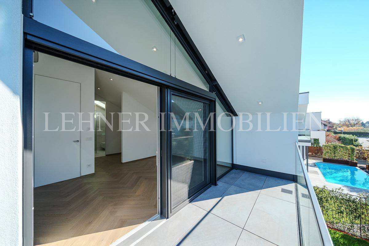 Geräumiger Balkon mit Fliesenboden, Glasgeländer und Blick auf den Poolbereich.