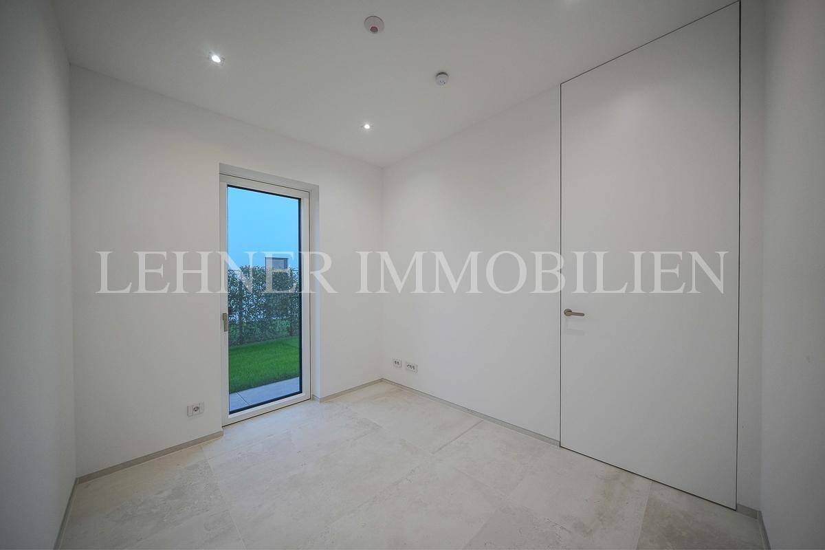 Helles Zimmer mit Fliesenboden, großer Fenstertür und minimalistischer weißer Tür.