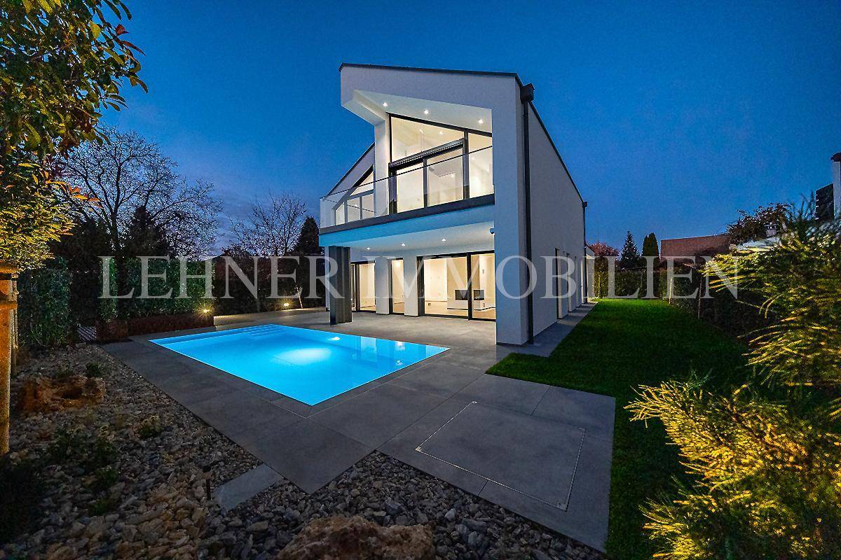 Moderne Villa mit beleuchtetem Pool und gepflegtem Gartenbereich in der nächtlichen Ansicht.