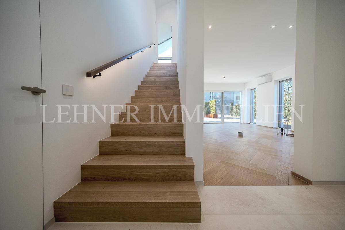 Heller Eingangsbereich mit moderner Holztreppe und Blick in den offenen Wohnbereich.