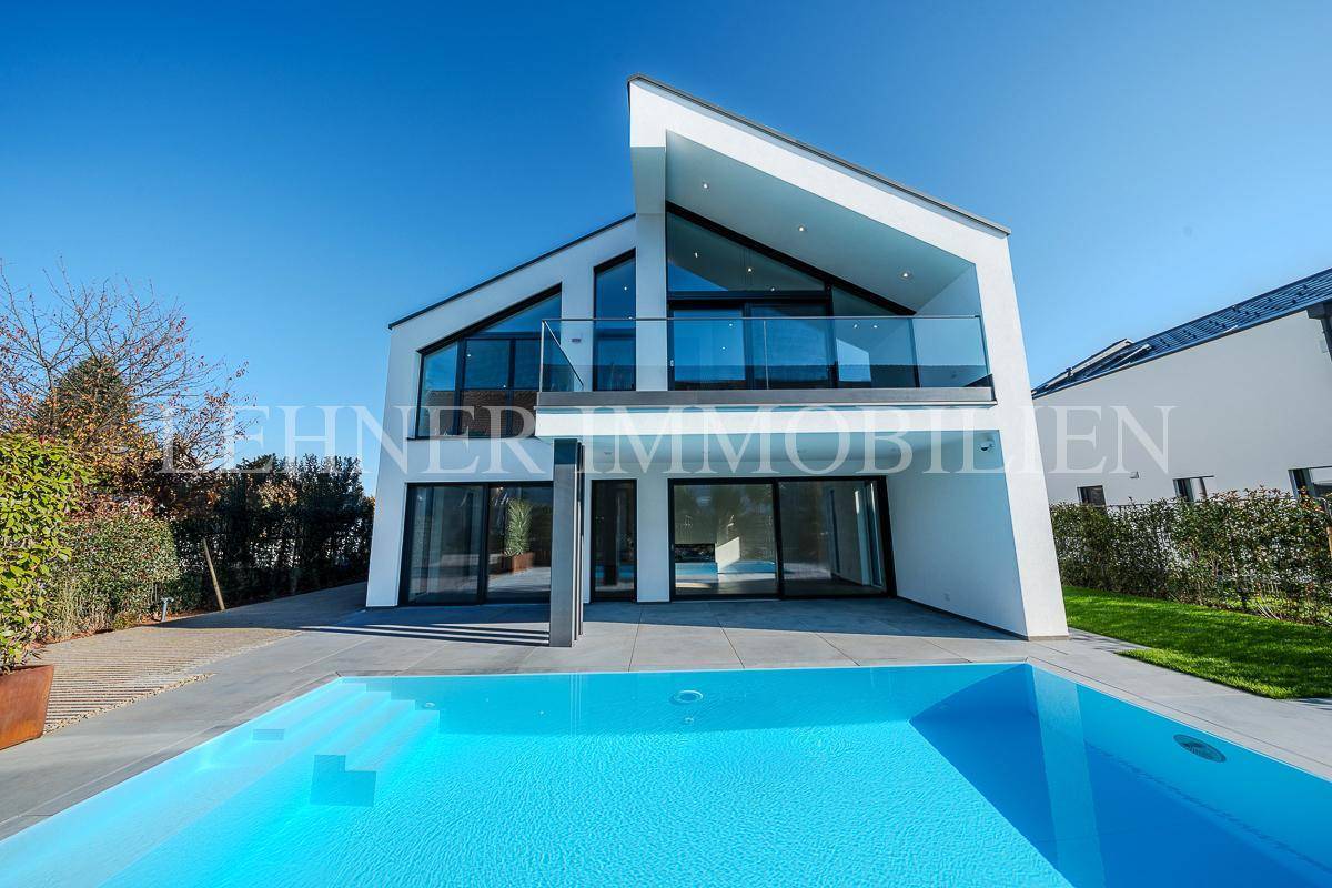 Moderne Villa mit großem Pool und weitläufiger Terrasse unter strahlend blauem Himmel.