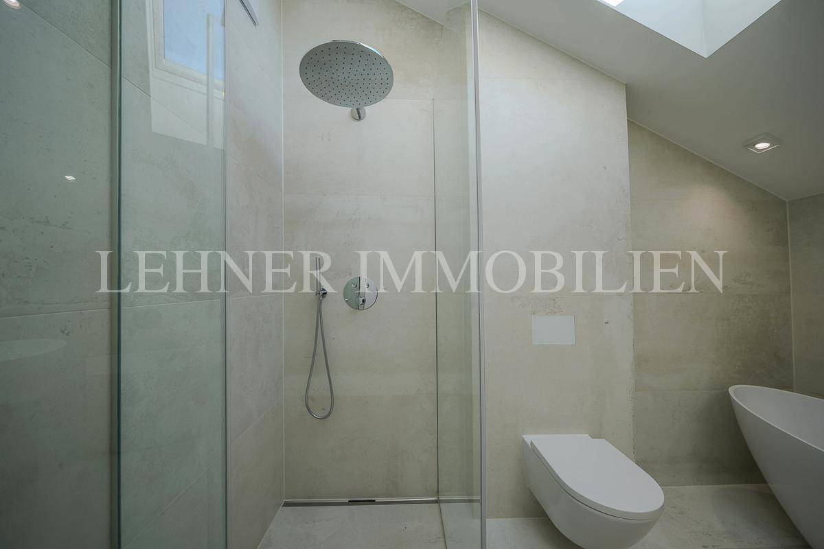 Moderne Duschkabine mit Regendusche, Wand-WC und hellem Fliesenboden.