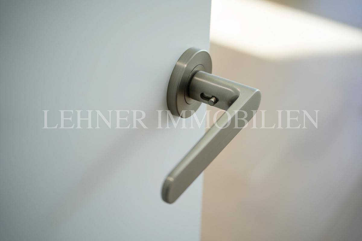 Nahaufnahme eines modernen, gebürsteten Türgriffs aus Metall an einer weißen Tür.
