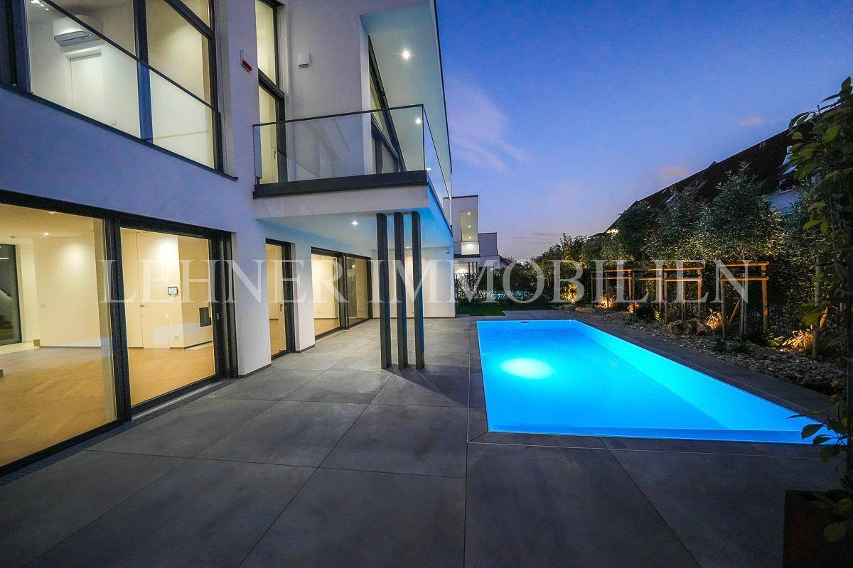Großzügiger Poolbereich mit Terrasse und Blick auf die moderne Architektur der Villa bei Nacht.