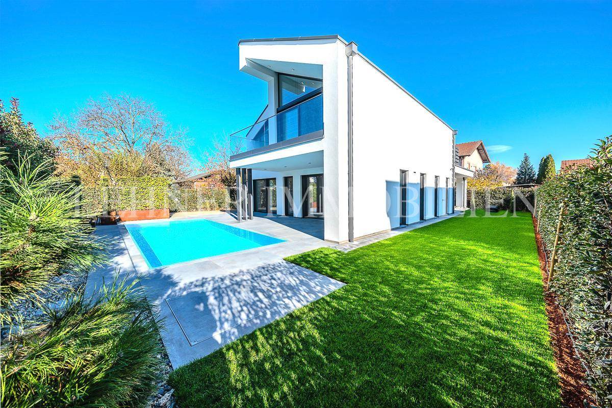 Seitliche Ansicht der modernen Villa mit Pool und weitläufiger Rasenfläche im sonnigen Garten.