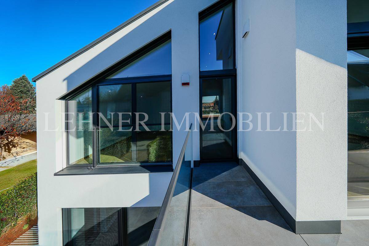Moderne Architektur mit großen, schrägen Fenstern und Balkon mit Glasgeländer.
