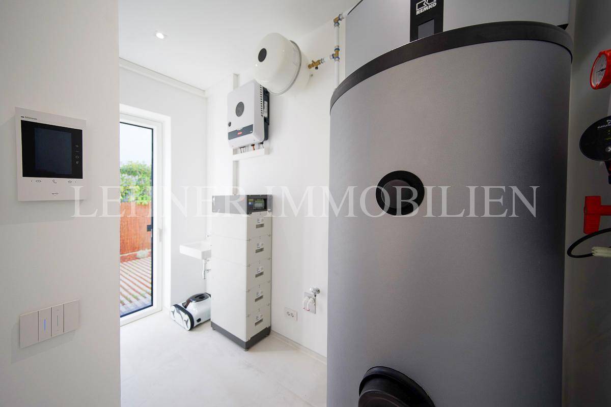 Technikraum mit Warmwasserspeicher, Steuerungseinheiten und Fenster zum Außenbereich.