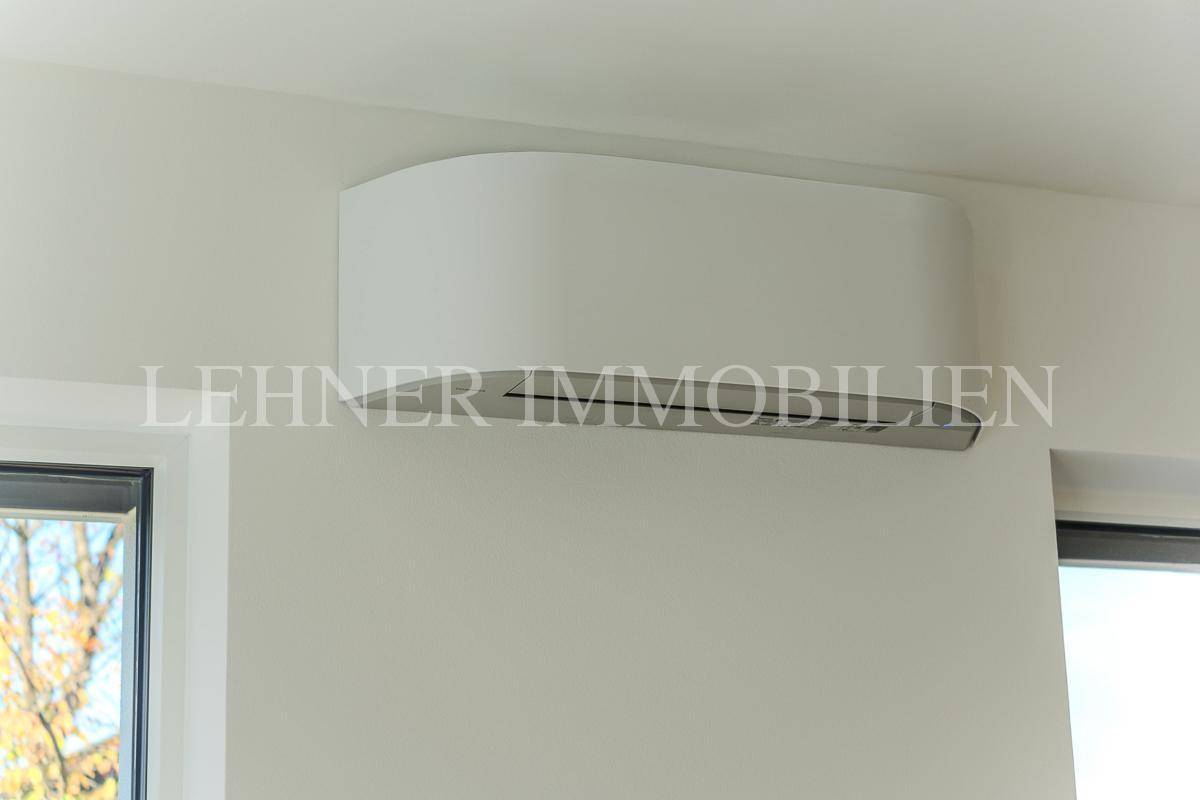 Moderne Klimaanlage an der Wand in einem hellen Innenraum mit großen Fenstern.