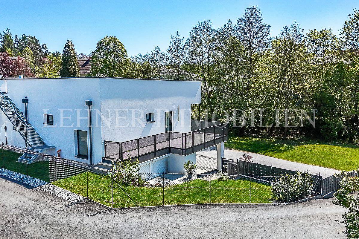 Rückansicht eines modernen Hauses mit Treppe, Rasenfläche und Balkon, umgeben von Bäumen.