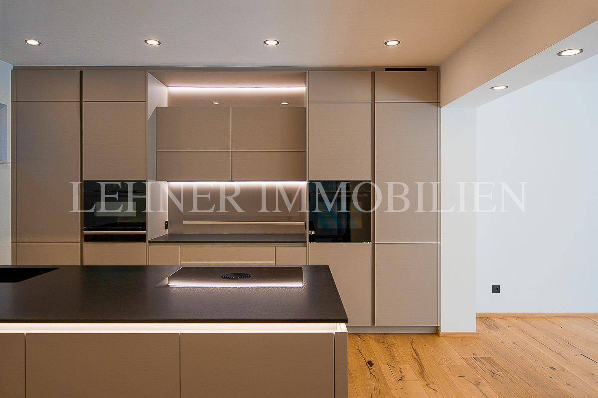 Moderne Einbauküche in Beige mit integrierten Geräten, Kochinsel und Holzboden in einem offenen Raum.