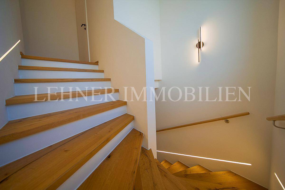 Moderne Holztreppe mit integrierter LED-Beleuchtung und schlichtem Holzgeländer in einem hellen Treppenhaus.