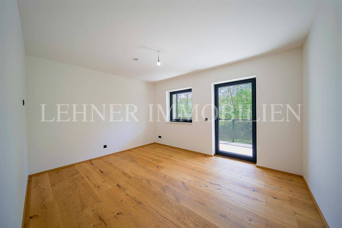 Geräumiges Wohnzimmer mit Holzboden, weißen Wänden und großen Fenstern für viel Tageslicht.