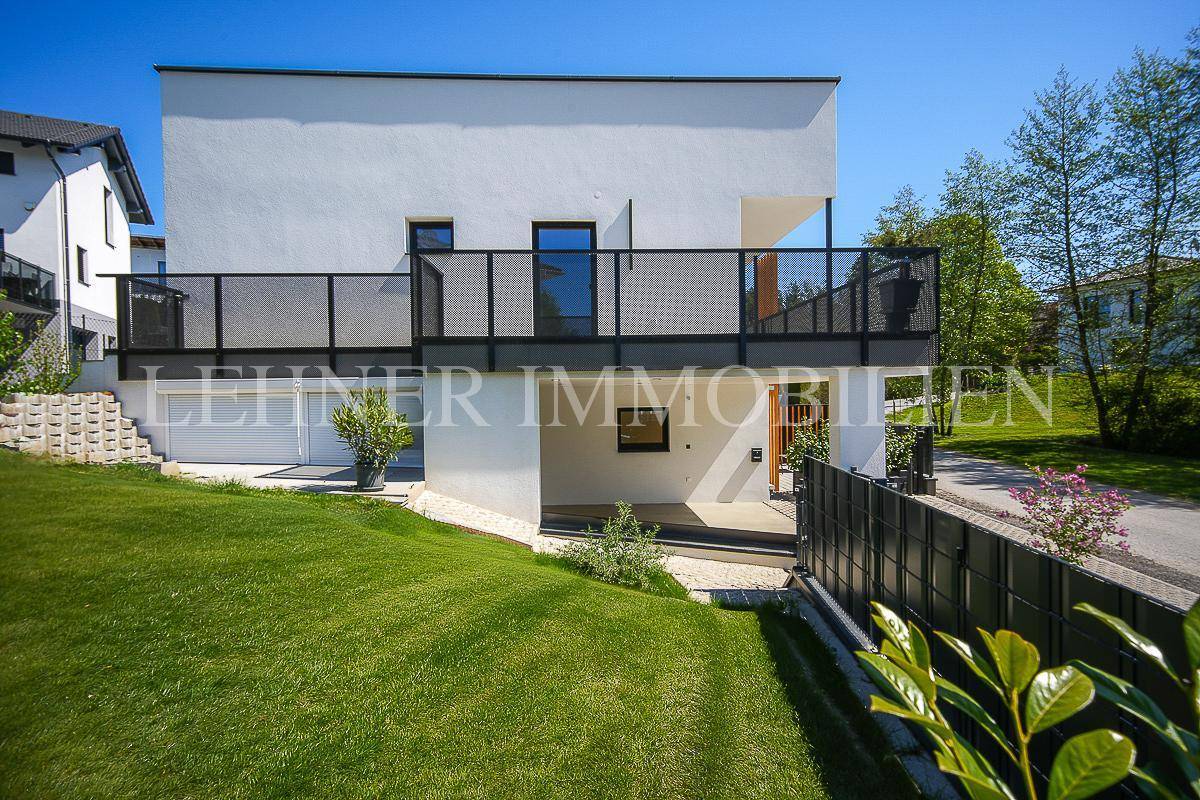 Seitenansicht eines modernen Hauses mit Rasenfläche und Balkon, umgeben von Natur.