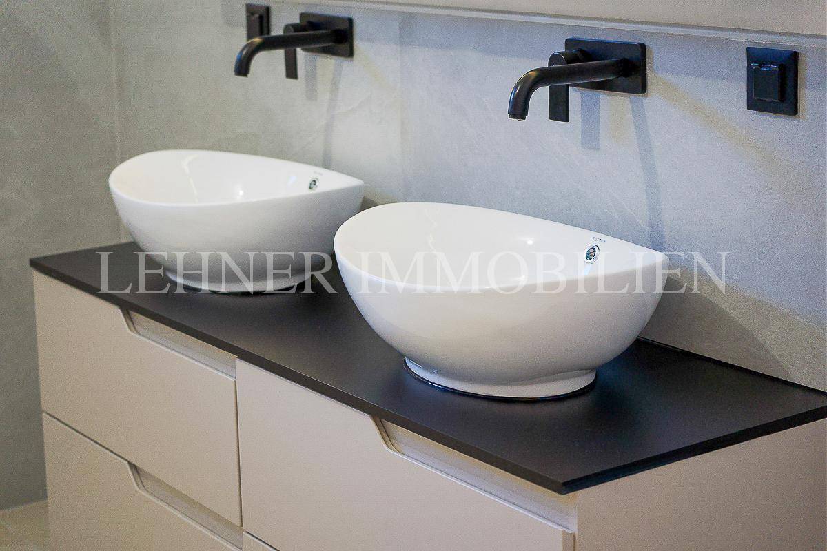 Modernes Badezimmer mit Doppelwaschbecken, schwarzen Armaturen und eleganten Fliesen.