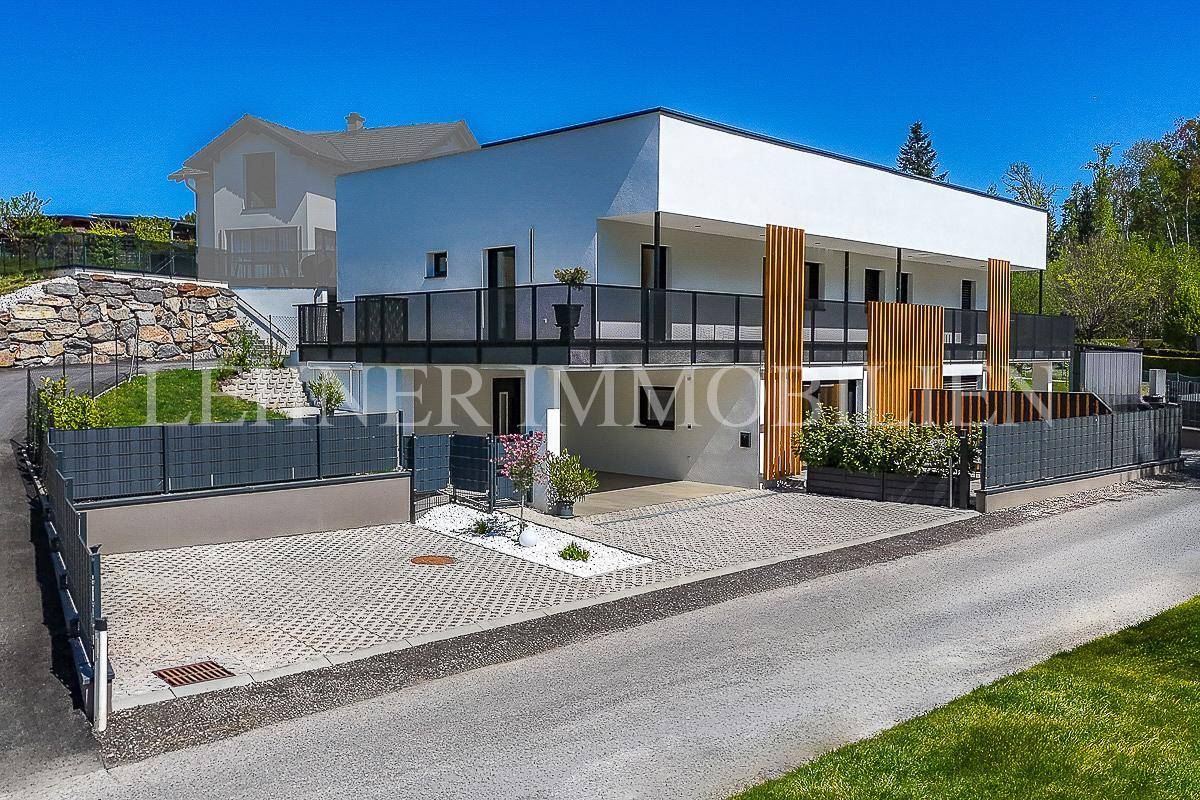 Modernes Mehrfamilienhaus bei Tag mit weißer Fassade und Balkonen, umgeben von Grünflächen.