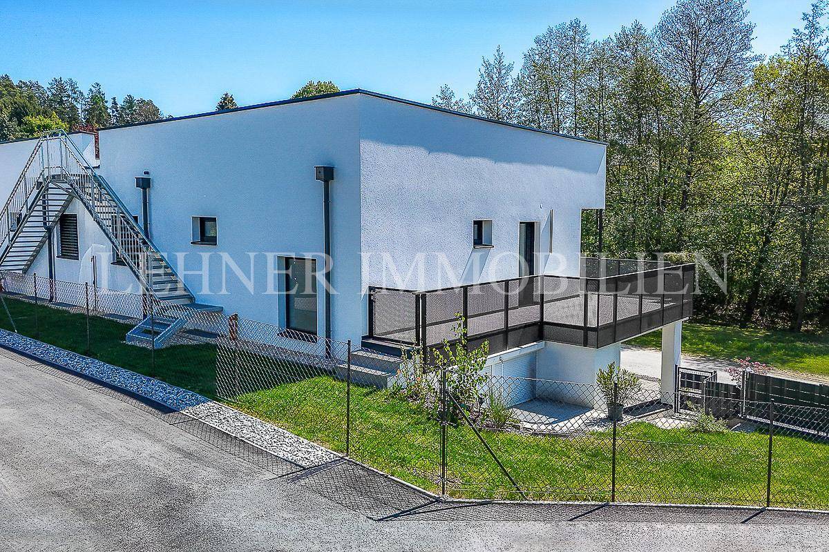 Modernes Einfamilienhaus mit weißer Fassade, Balkon und Treppenaufgang im Grünen.