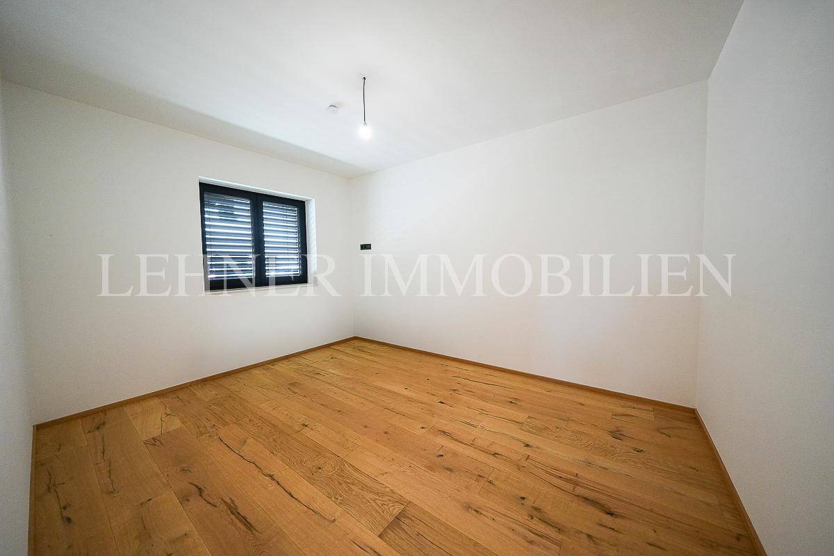 Schlafzimmer mit Holzboden, weißen Wänden und einem Fenster mit Jalousien für Privatsphäre.