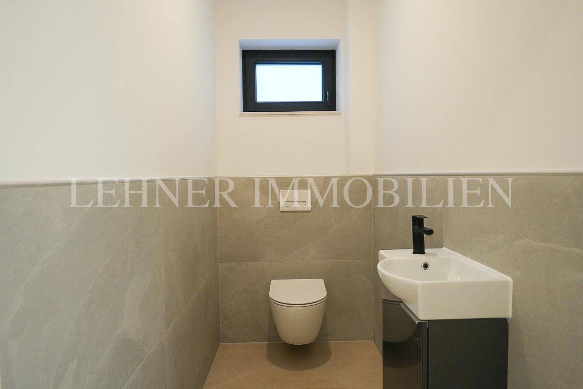 Modernes Gäste-WC mit Wand-WC, kleinem Waschbecken und Fenster für natürliche Belüftung.