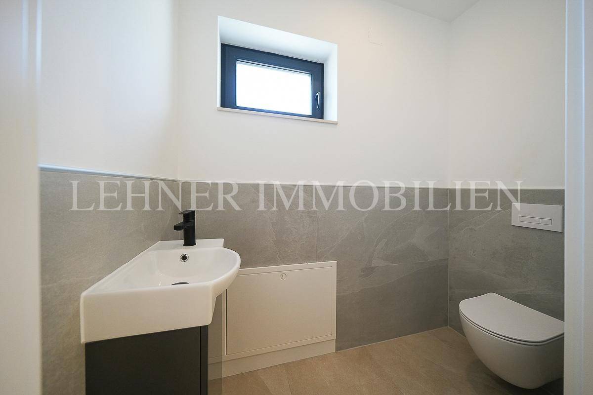 Modernes Gäste-WC mit Wand-WC, kleinem Waschbecken und Fenster für natürliche Belüftung.