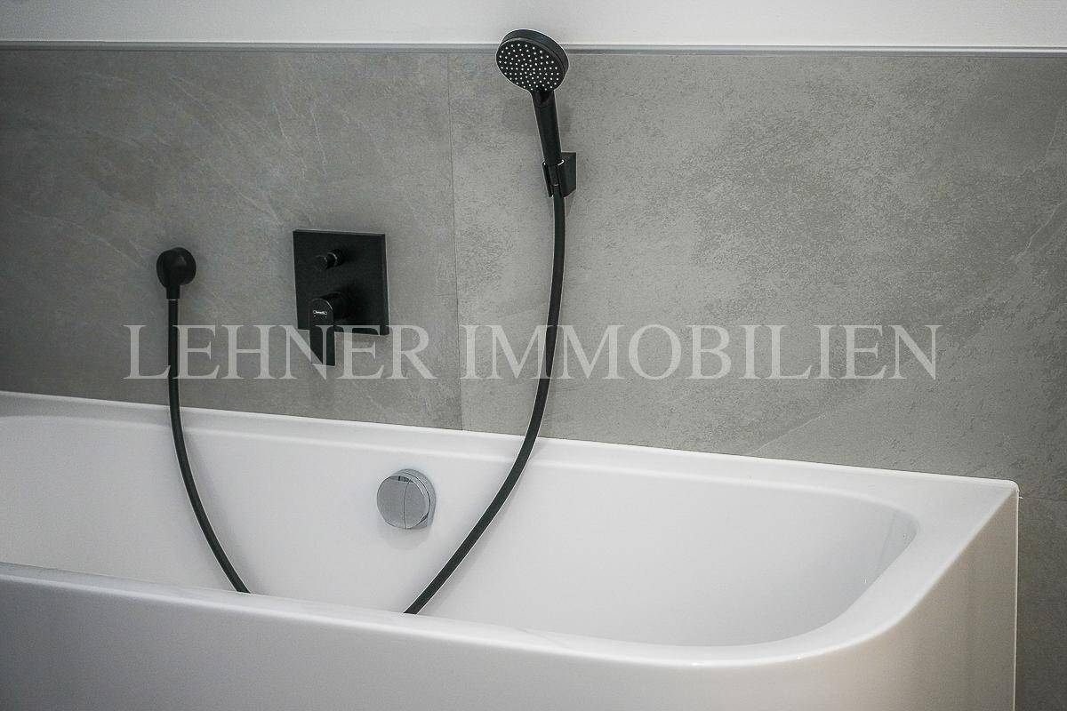 Detailansicht der modernen Badewanne mit schwarzen Armaturen und Handbrause.