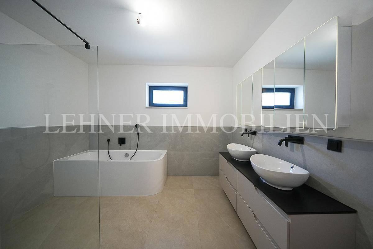 Geräumiges Badezimmer mit Badewanne, Doppelwaschbecken, großer Spiegelfront und Fenster.