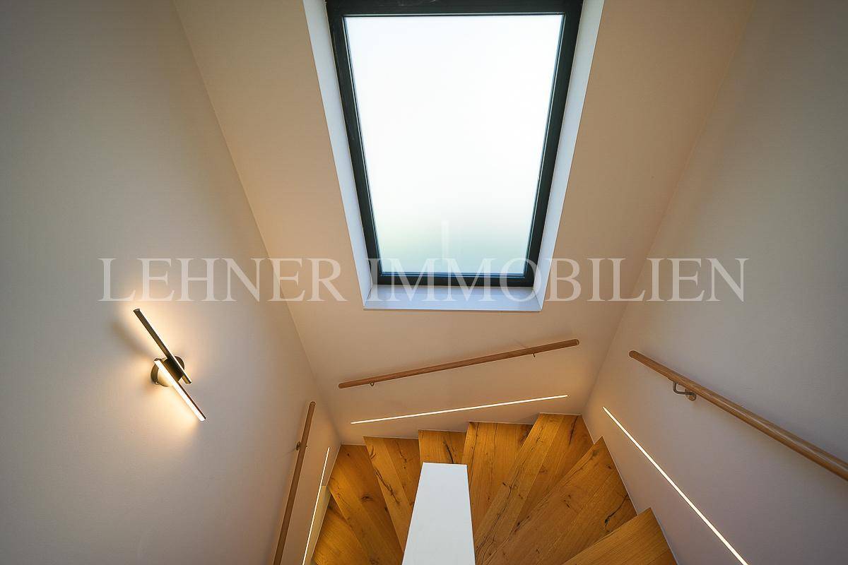 Heller Treppenaufgang mit Holzstufen, Holzgeländer und einem großen Dachfenster für viel Tageslicht.