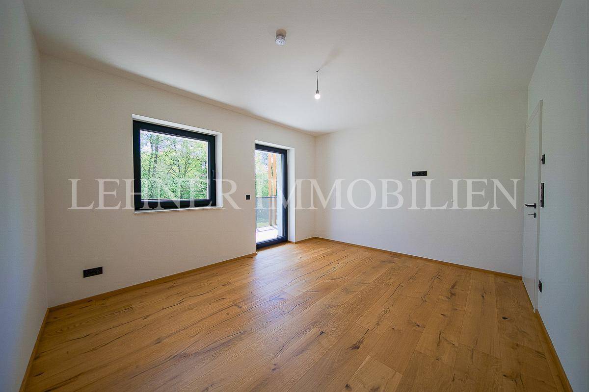 Helles Schlafzimmer mit Holzboden, weißen Wänden und Zugang zu einem Balkon oder Garten.