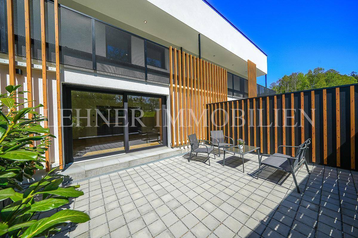 Helle Terrasse mit Sitzgelegenheiten und Blick auf die moderne Fassade bei Tageslicht.