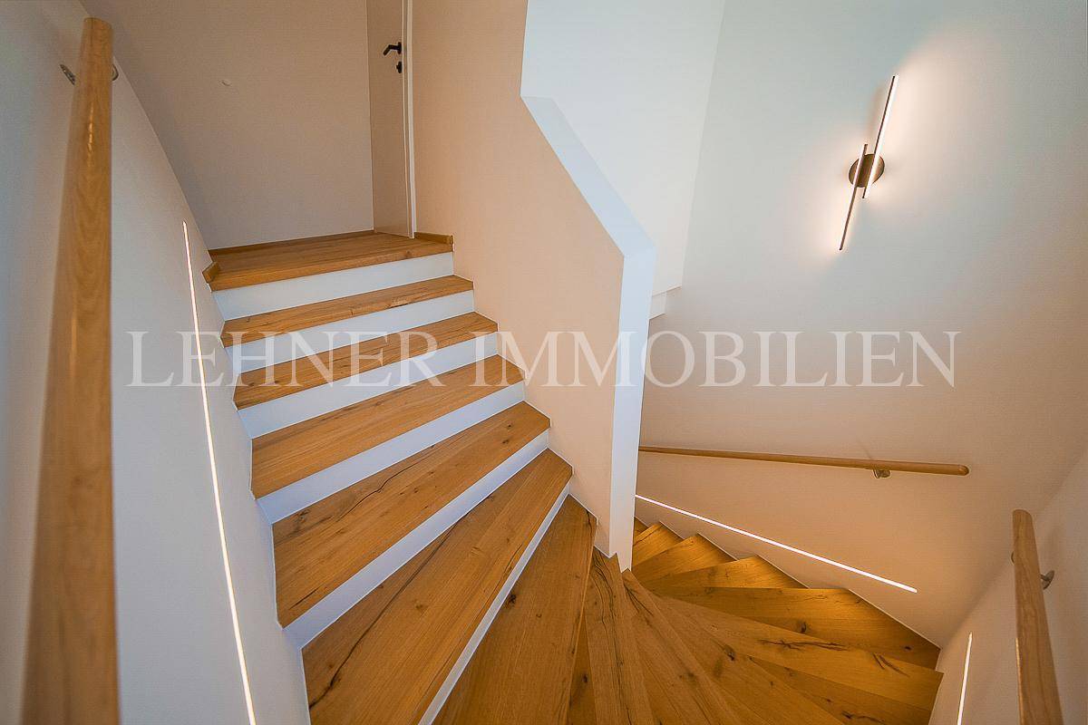 Elegante Holztreppe mit indirekter Beleuchtung und minimalistischem Design, die zu den oberen Etagen führt.