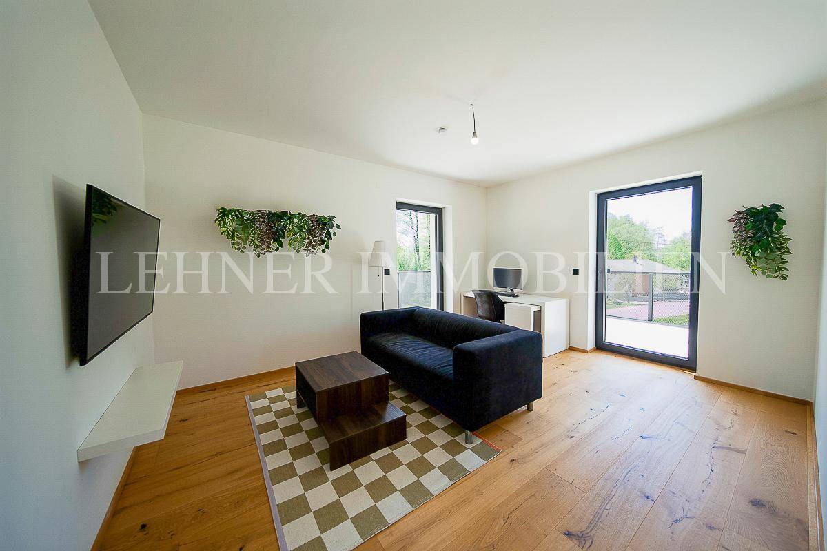 Helles Wohnzimmer mit Holzboden, schwarzem Sofa und Zugang zu einem Balkon oder Garten.