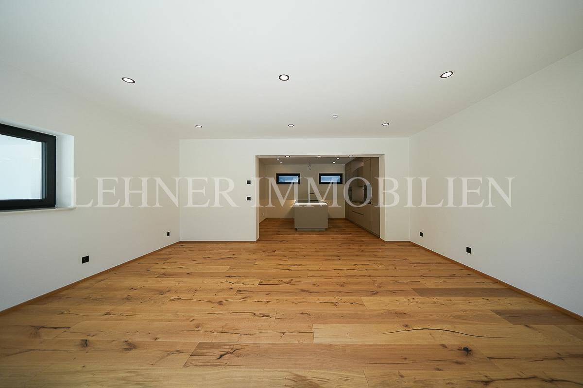 Geräumiges Wohnzimmer mit hellem Holzboden und offener Verbindung zur Küche, modern gestaltet.