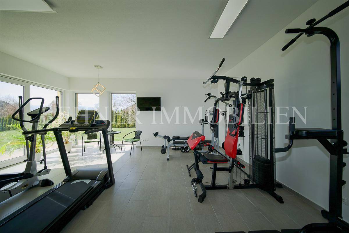Geräumiger Fitnessraum mit verschiedenen Trainingsgeräten und Blick in den Garten.