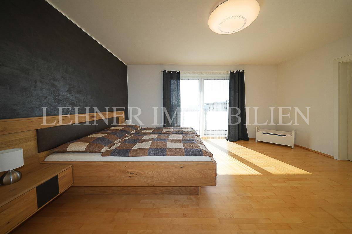 Modernes Schlafzimmer mit Holzbett, dunkler Akzentwand und Zugang zum Balkon.