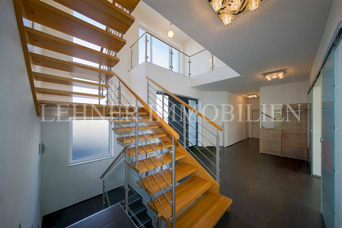 Elegante Holztreppe mit Edelstahlgeländer in einem hellen, offenen Treppenhaus.