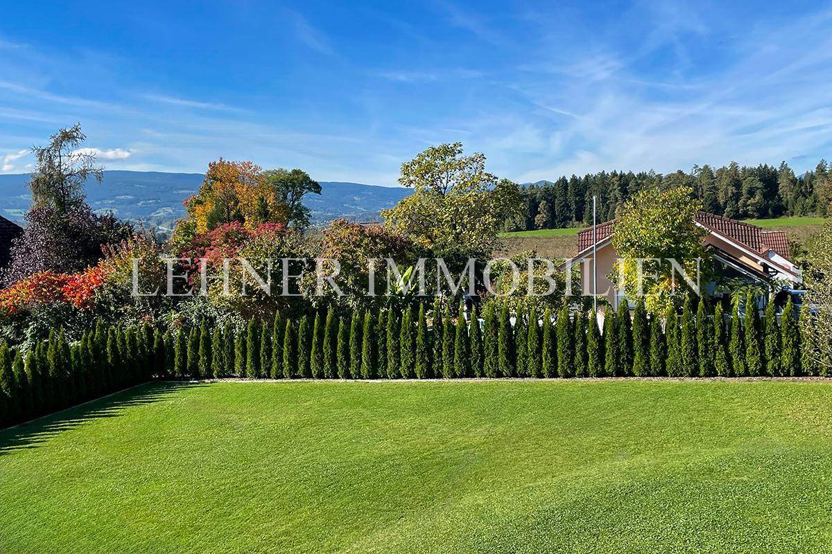 Gepflegter Garten mit hoher Hecke und weitem Blick auf die umliegende Natur und Hügel.