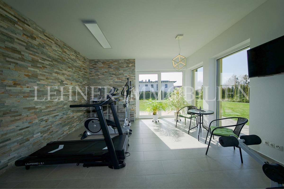 Moderner Fitnessraum mit Steinwand, großen Fenstern und Zugang zum Garten.