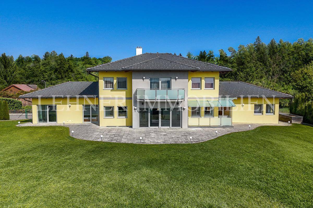 Modernes Einfamilienhaus mit gelber Fassade, großem Garten und Balkon bei Tageslicht.