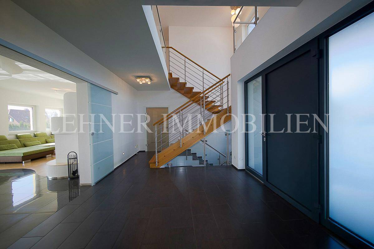 Moderner Eingangsbereich mit dunklem Fliesenboden, offener Treppe und Zugang zum Wohnzimmer.