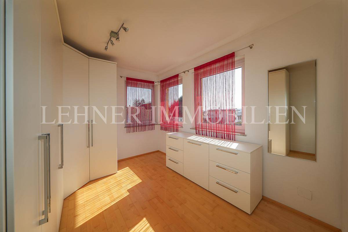 Freundliches Schlafzimmer mit Holzfußboden, weißen Möbeln und roten Vorhängen.