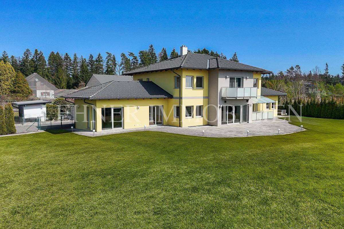 Rückansicht des modernen Hauses mit weitläufigem Garten, Terrasse und Balkon.